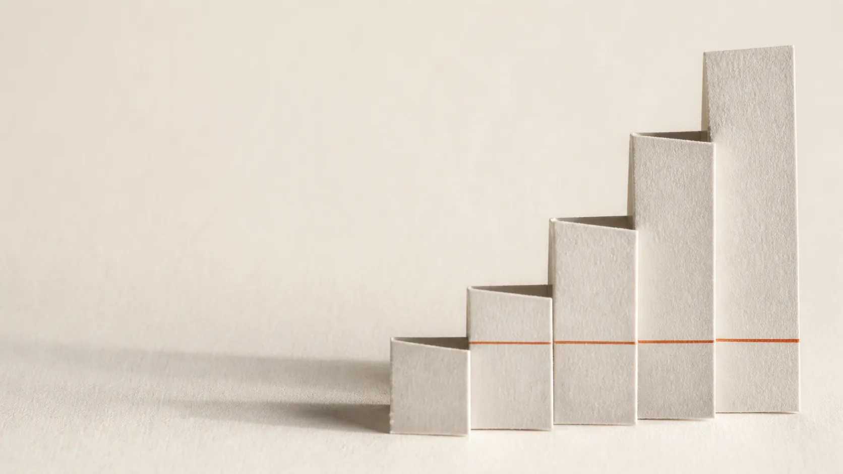 Paper folded into ascending steps of unequal height with a single fine terracotta line running across them as a measured baseline.
