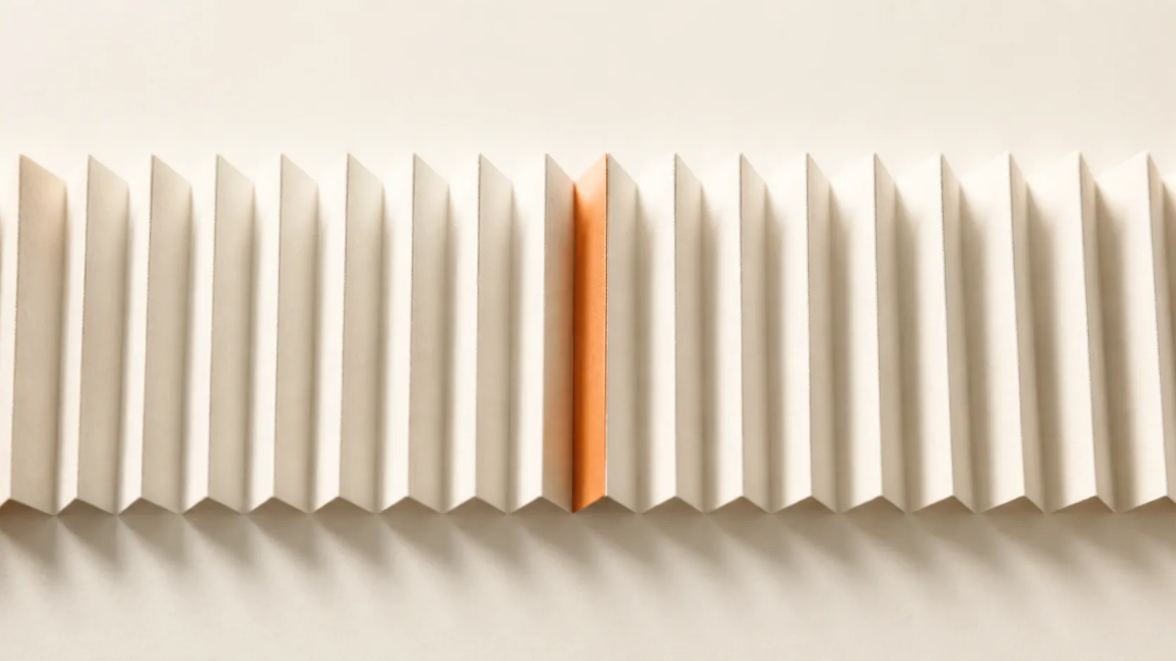 An even accordion of identical paper folds running the full width, one crease in terracotta, reading as a system rather than an object.