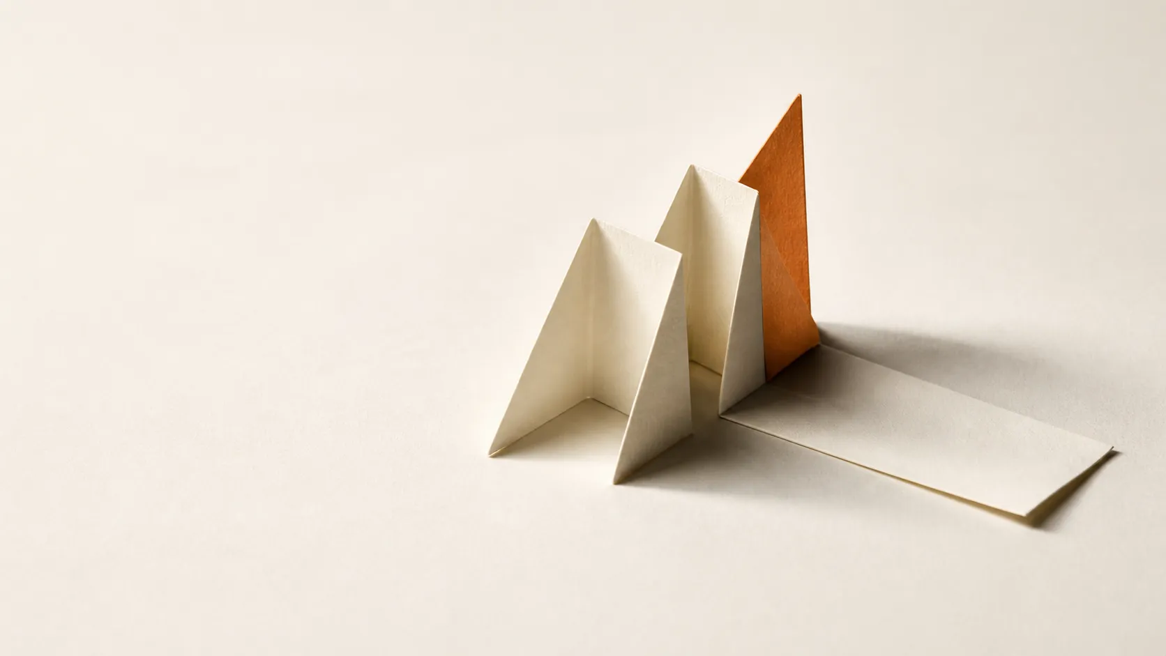 Folded paper climbing in three accordion peaks, the tallest in terracotta, then collapsing flat into a long tail.